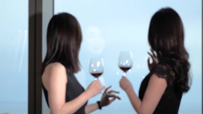 两位美女窗边洽谈碰杯喝红酒