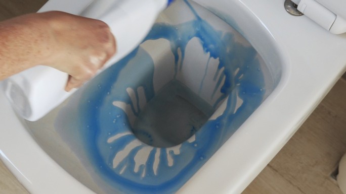 用蓝色清洁液清洁浴室中的白色马桶