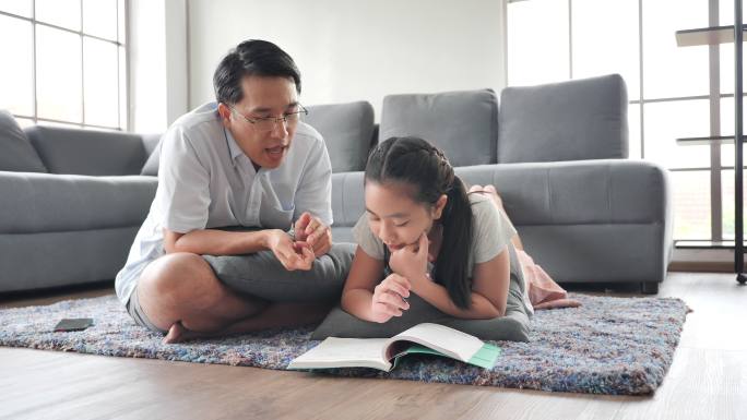 父亲在客厅的地板上教女儿读书。