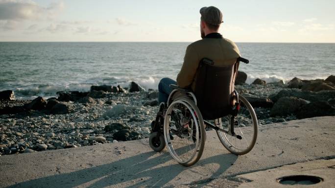 孤独的人坐在海边的轮椅里，遥望远方