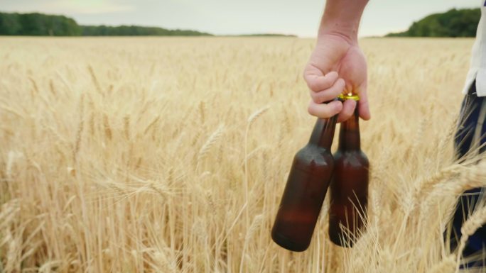 一个男人拿着两瓶冷啤酒走过一片大麦地