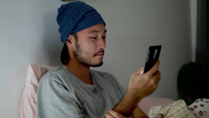男人躺在家里的床上使用智能手机。