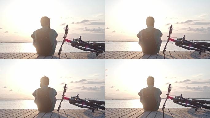 日落时骑自行车坐在海边的男子。