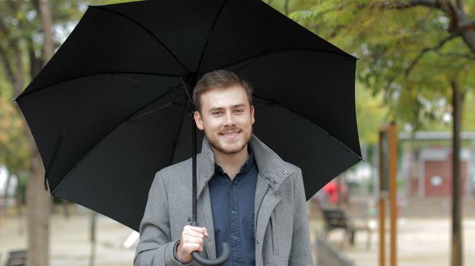 男人在雨中走在公园里，手里拿着雨伞