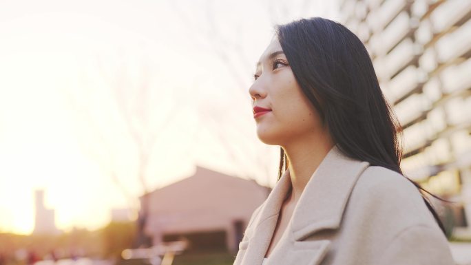 年轻都市女性阳光下昂首站在小区公园