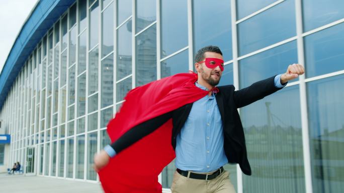 企业家穿着超人服装披肩，戴着面具在户外跑