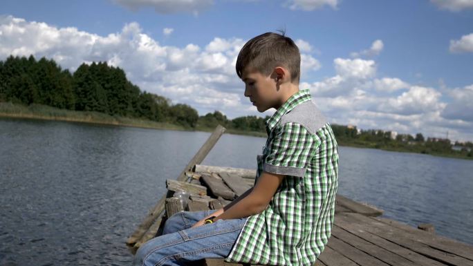 男孩坐在湖边的码头上