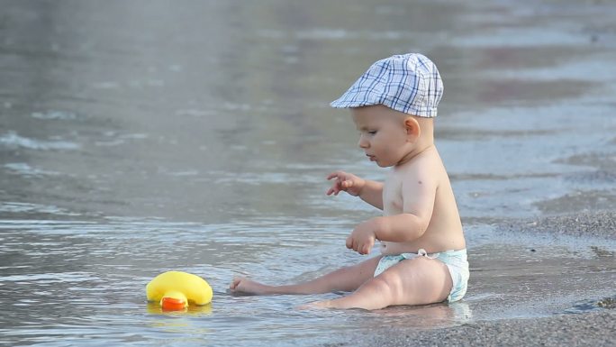 坐在海岸上的小婴儿，正在玩鸭子玩具