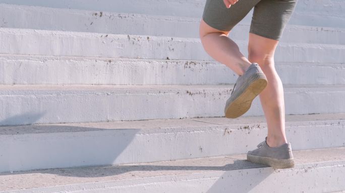 穿着灰色鞋子的快乐的年轻女子跑上楼梯。