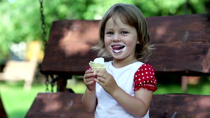 小女孩坐在秋千椅上吃冰淇淋，笑嘻嘻的。