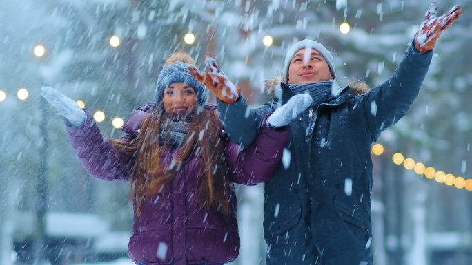 一对穿着夹克戴着帽子的情侣在冬季公园玩雪