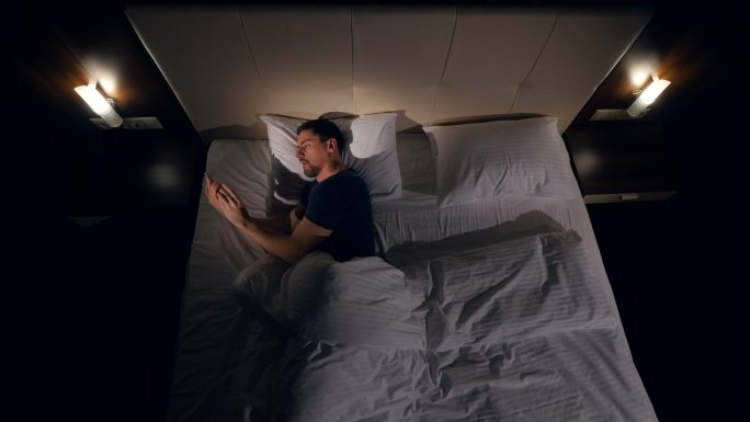 一名男子在黑暗中躺在床上使用智能手机