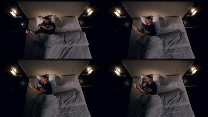 一名男子在黑暗中躺在床上使用智能手机