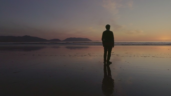 日落时一名男子站在海边的镜头