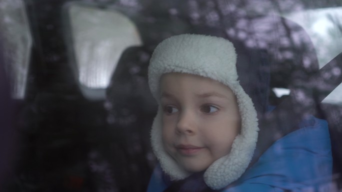 小男孩坐在汽车后座上，看着窗外。