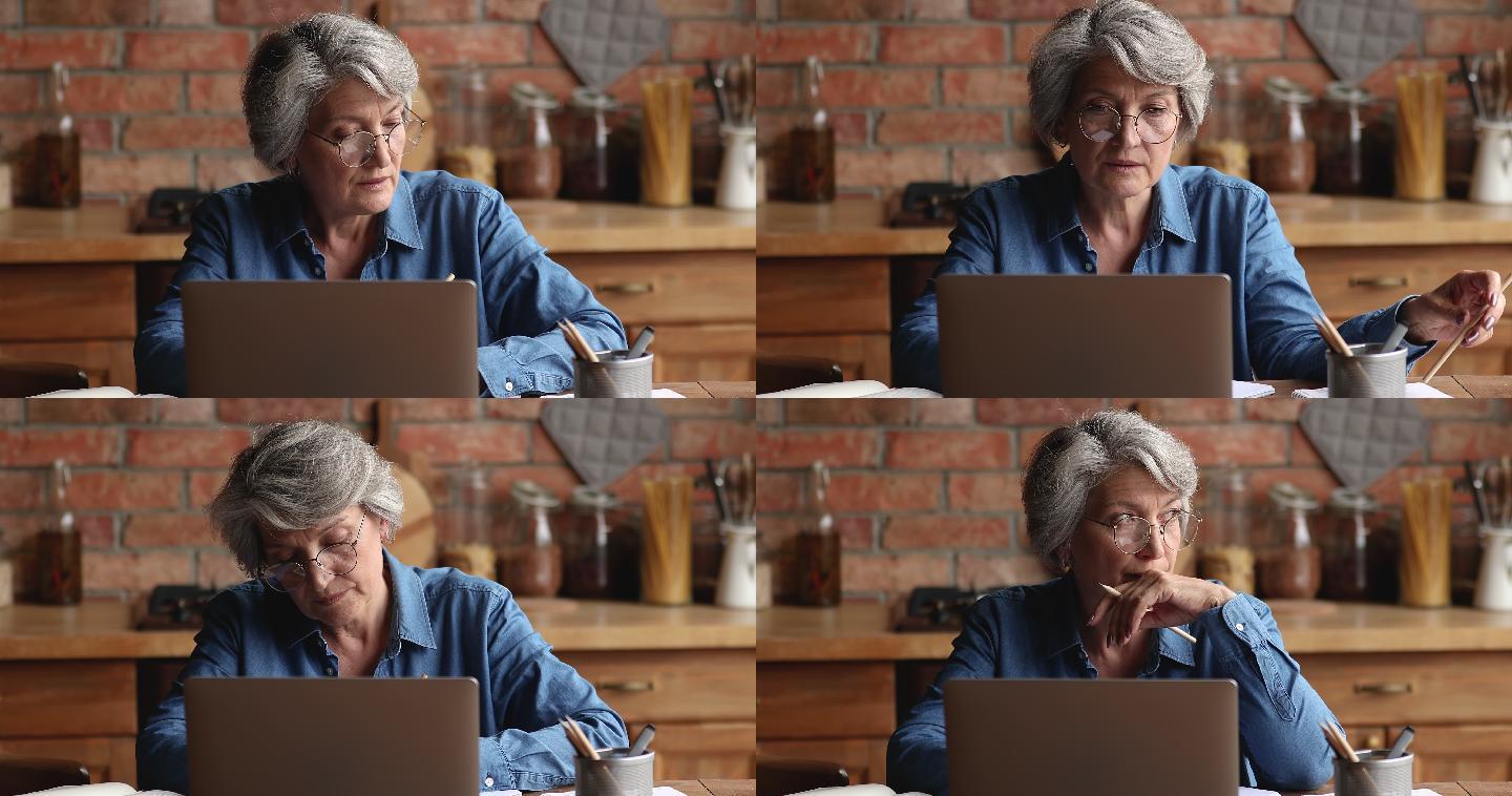 沉思的老妇人坐在室内在笔记本电脑上工作