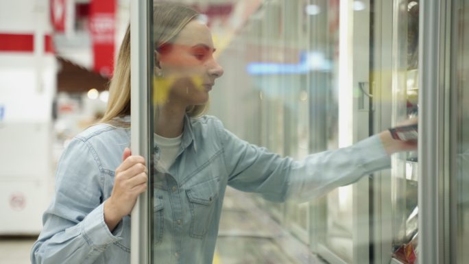 在超市购物的妇女选择冰箱里的冷冻产品