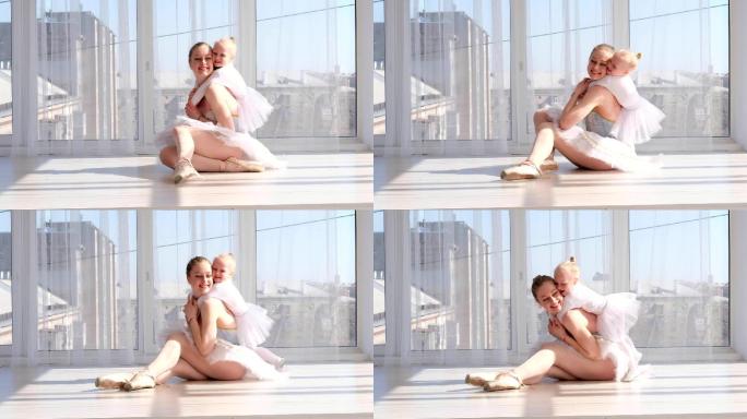 年轻的母亲在芭蕾舞演播室拥抱微笑的小女儿