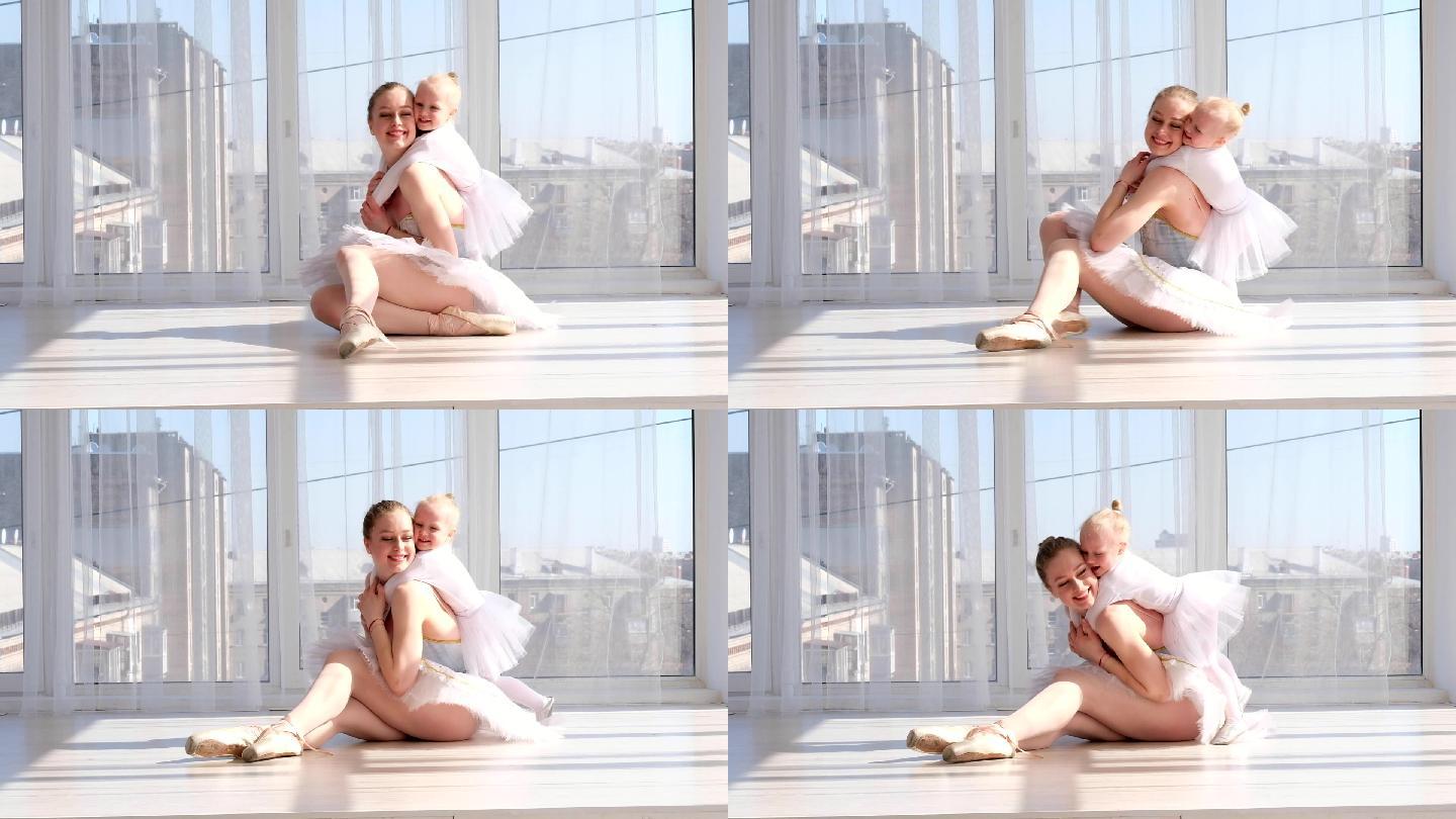 年轻的母亲在芭蕾舞演播室拥抱微笑的小女儿