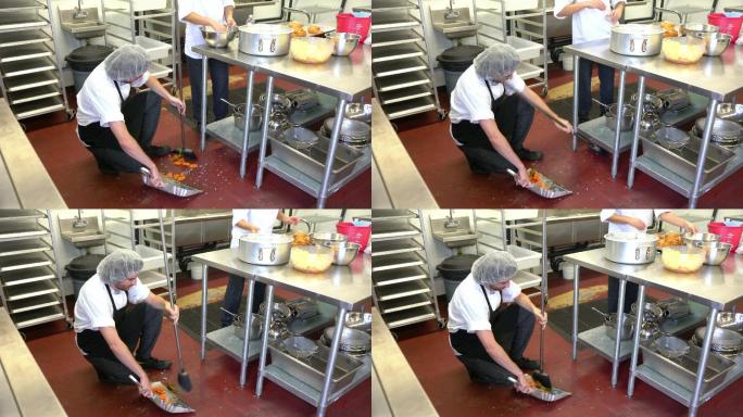 一名服务员正在清理商业厨房里凌乱的地板
