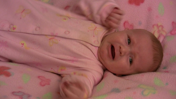 穿着粉红色衣服的女婴在毯子上哭泣