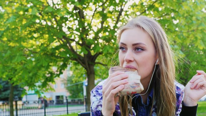 女人在公园里吃三明治，听音乐