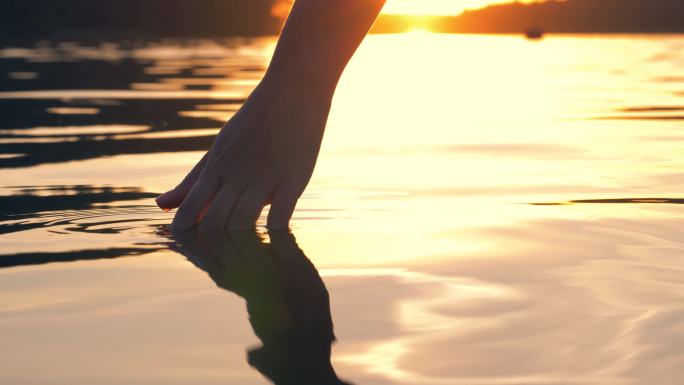 在金色的夕阳中，手轻轻地触摸着水面