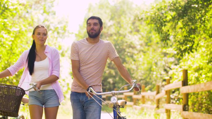 一对夫妇推着自行车沿着夏季公园散步