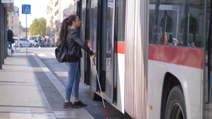 年轻的盲人妇女拿着手杖上了公共汽车。
