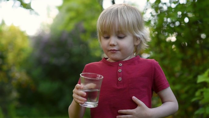 小男孩在后院或家中花园里喝一杯水