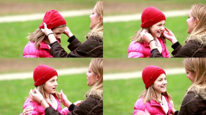 妈妈把帽子戴在女儿的头上并亲吻她的额头