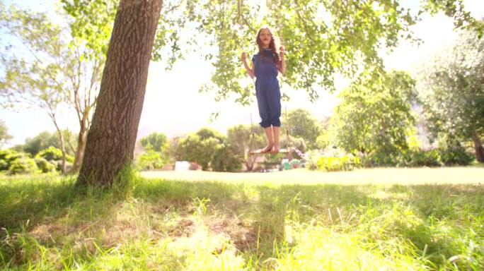 一个女孩站在大树下的秋千上