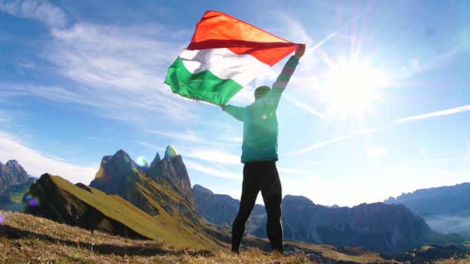 年轻人站在山顶上向天空升起意大利国旗