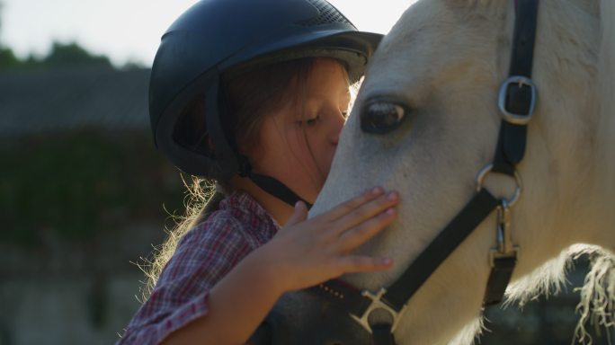 可爱小女孩在马厩里爱抚一匹白色小马。