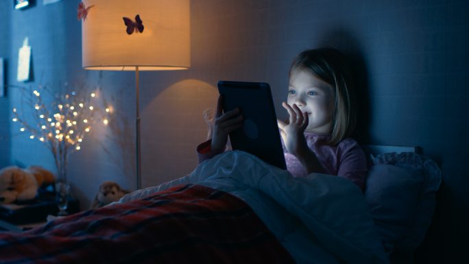 卧室里小女孩躺在床上玩平板电脑