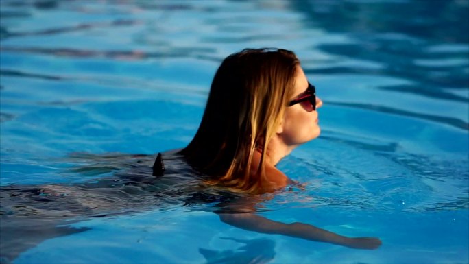 一个戴着墨镜的金发女人在泳池游泳