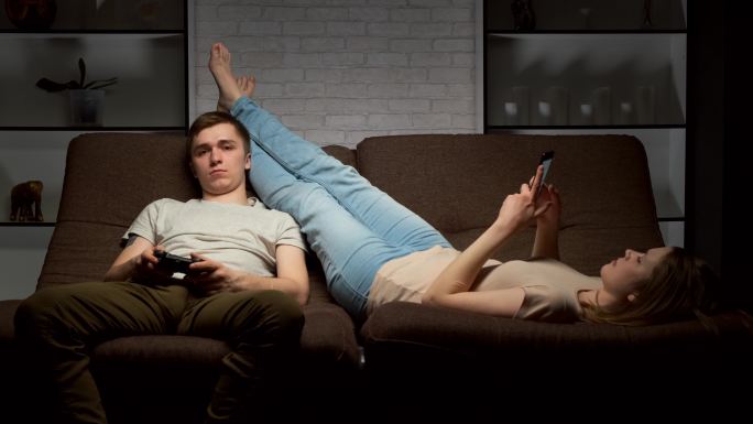 男子在玩电子游戏，女朋友在使用智能手机。