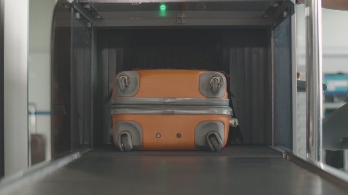 橙色行李箱从机场扫描仪中取出