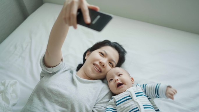 年轻母亲和婴儿躺在床上用手机自拍