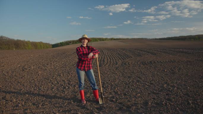 女农民站在田里，手里拿着铲子