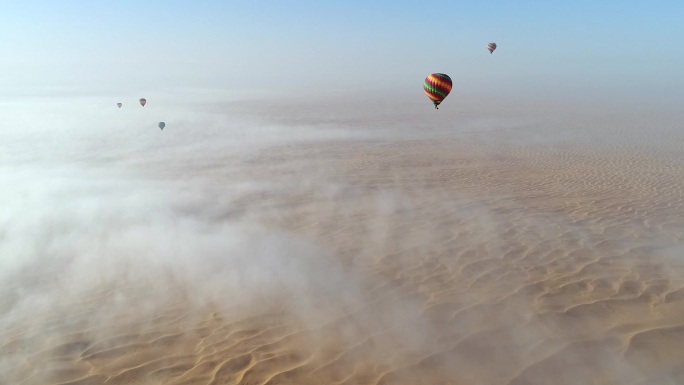 沙漠上的热气球在云层中飞行的鸟瞰图。