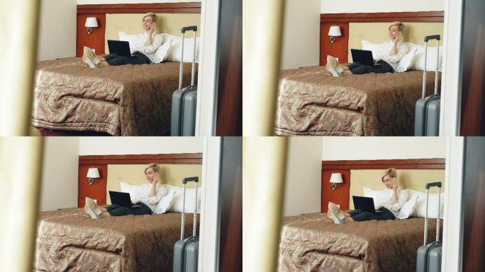 女人躺在酒店的床上使用笔记本电脑和手机