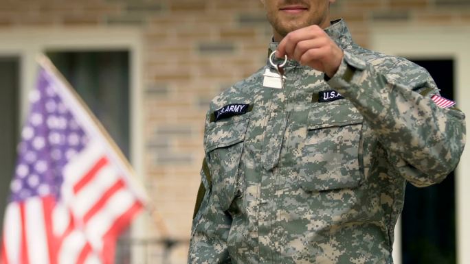美国士兵展示房屋钥匙站在建筑物外