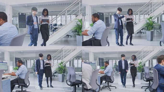 两位年轻的男女同事拿着平板电脑走进办公室讨论工作