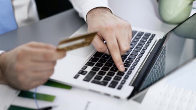 一个拿着信用卡在笔记本电脑上打字的男人