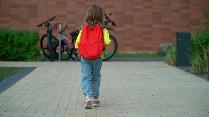 小女孩背着背包在校园里跑来跑去。