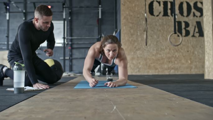 肌肉发达的女子在教练的指导下做平板支撑