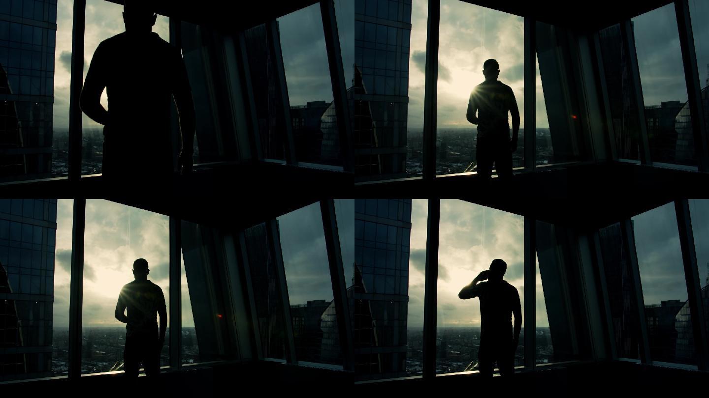 年轻人透过摩天大楼的窗户看城市和日落