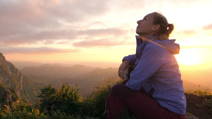 日出时分，坐在山顶上的女性欣赏高山风光。