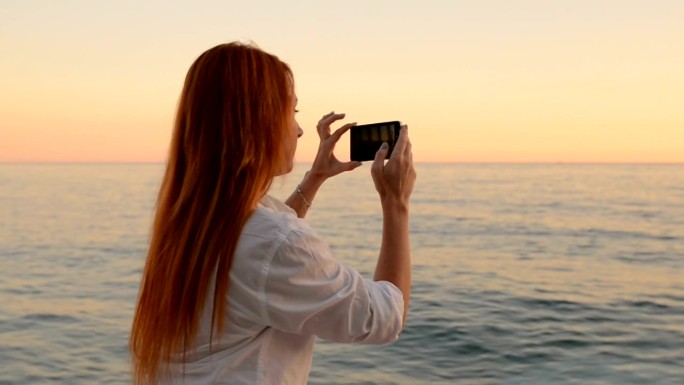年轻女子正在用手机摄像头拍摄海景